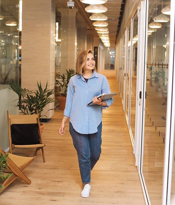 Imaginary femeie de birou zâmbitoare, cu tabletă în mână, într-un ambient modern și luminos.