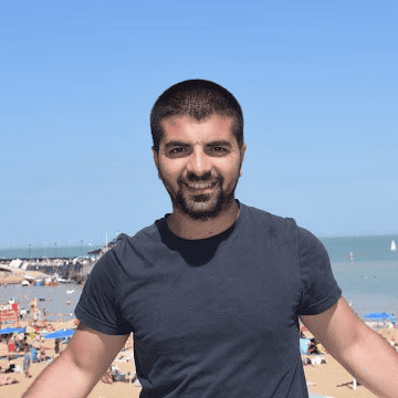 Tânăr zâmbind pe plajă cu mare și cer albastru în fundal.